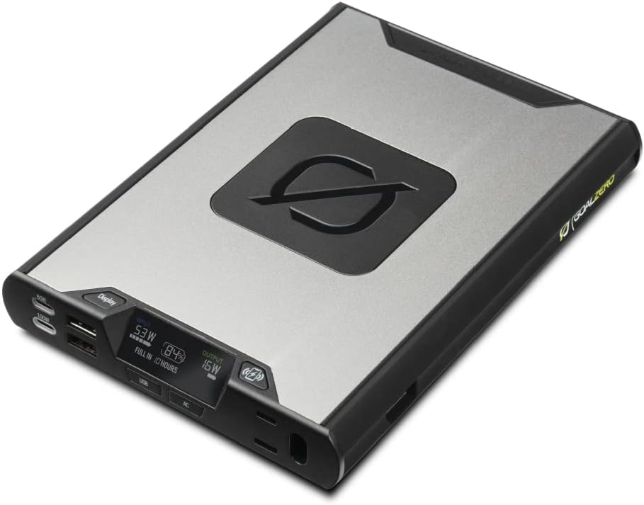 Goal Zero Sherpa 100AC 4th Generation power bank with color OLED display showing 100W output and a smartphone charging wirelessly on top.