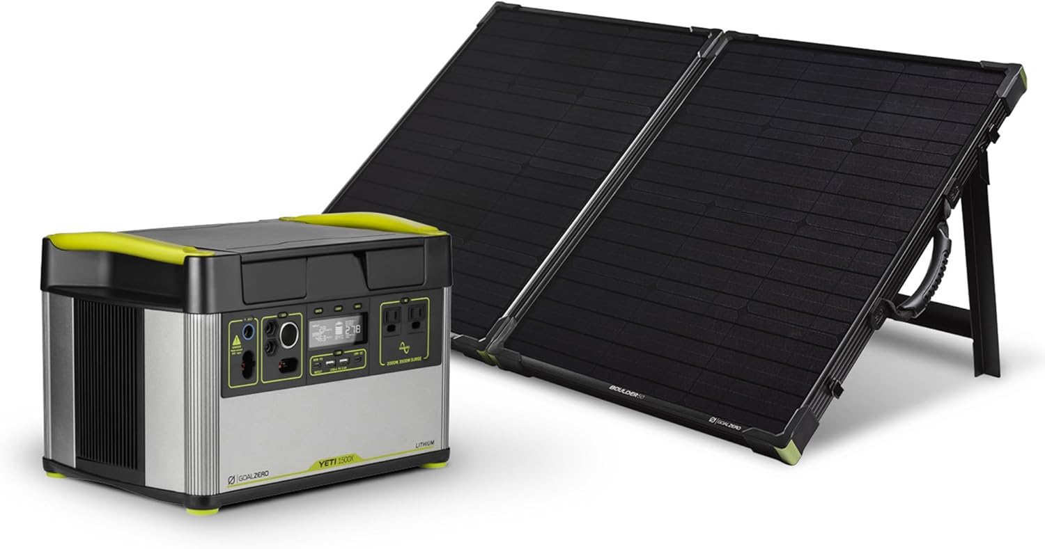 Goal Zero Yeti 1500X portable power station sitting on a wooden camping table with the Boulder 100 solar panel briefcase unfolded on the grass under the sun.