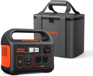 Jackery Explorer 300 Portable Power Station with carrying bag on a wooden camping table in the forest.