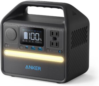 Anker 521 Portable Power Station with smart display and built-in light bar sitting on a wooden camping table in a forest.